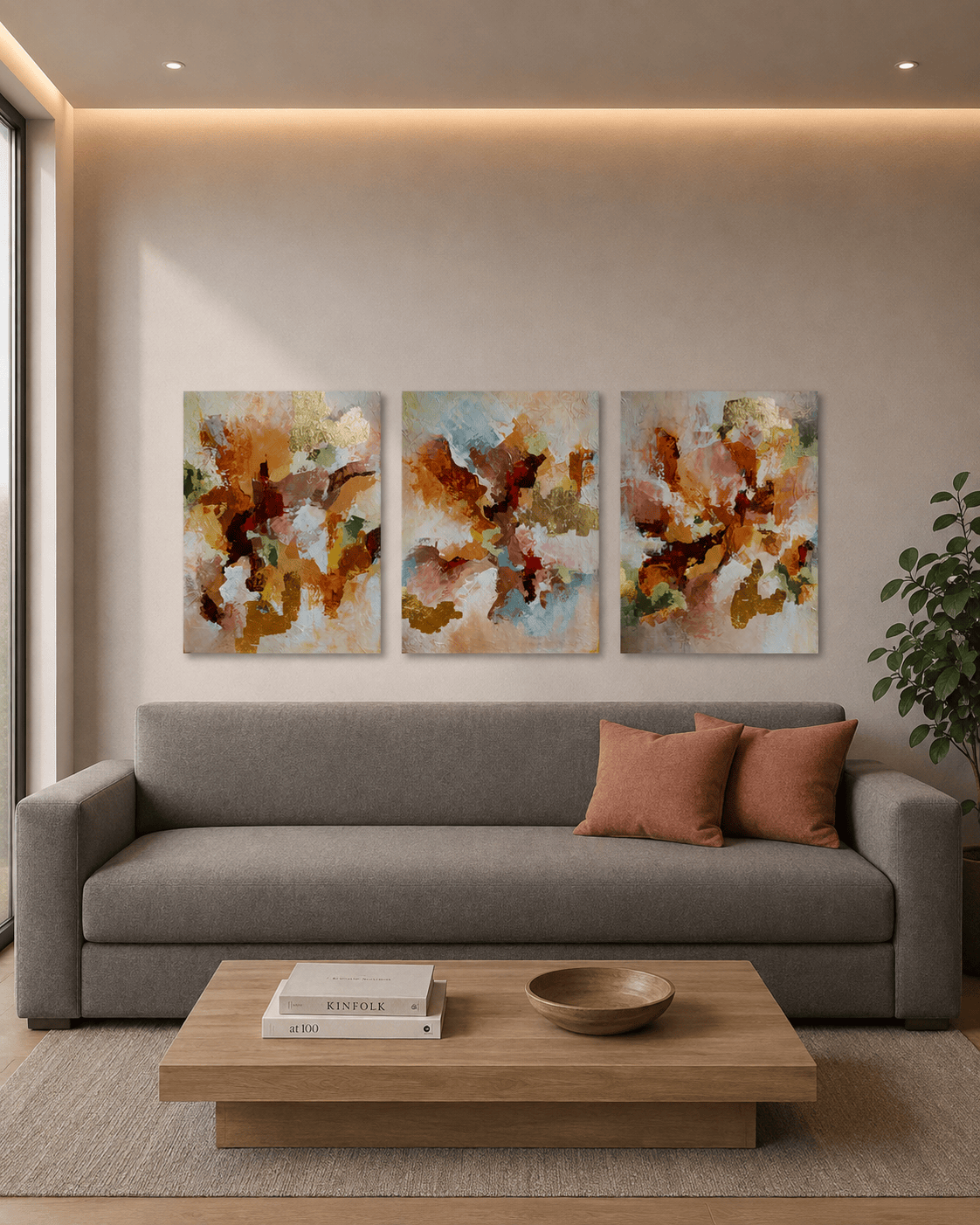 Ígnea 3 Conjunto de três quadros abstratos Ígnea, com cores quentes e detalhes em dourado, decorando a parede acima de um sofá cinza, em uma sala de estar moderna com almofadas terracota e mesa de centro em madeira clara.