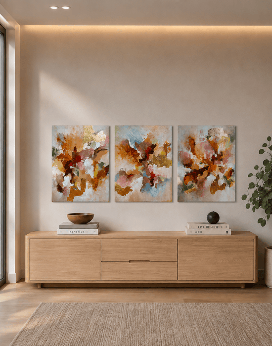 Tríptico de arte abstrata Ígnea, composto por três telas verticais em tons de terracota, laranja, rosa, azul e dourado, decorando a parede acima de um aparador de madeira clara em ambiente contemporâneo e minimalista.